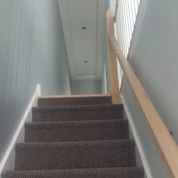 Indoor staircase with carpeted steps and a wooden handrail on the right side.