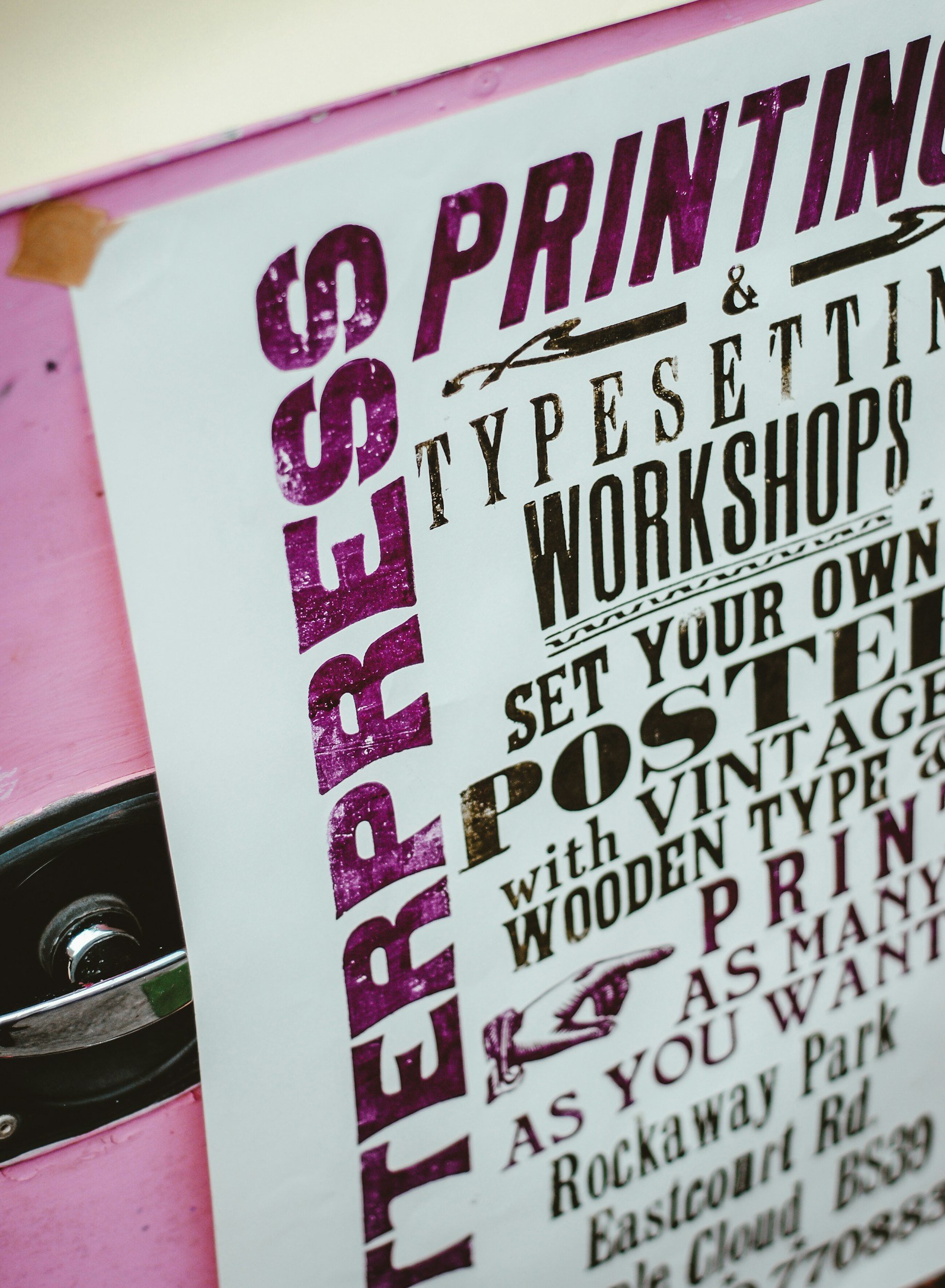 Close-up of a printed poster with bold black and purple text on a white background, partially visible. The poster appears to be advertising a workshop or class involving typography or printing.