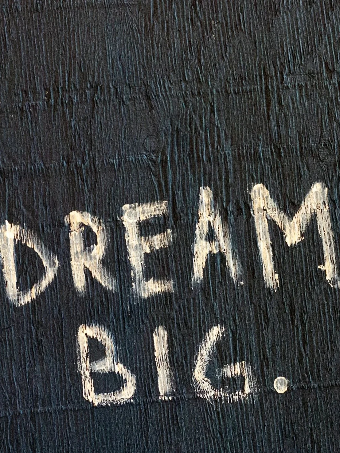 Close-up of a black surface with the words "Dream Big" written in white chalk.