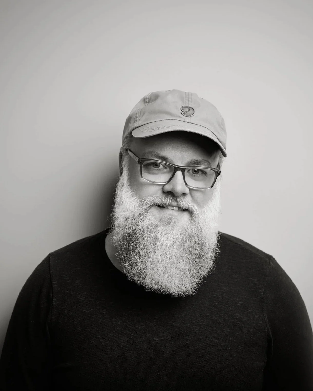 Schwarz-weiß-Fotografie von Andreas Krufczik. Eine Mann mit Brille, Vollbart und einer Mütze vor einem neutralen Hintergrund.