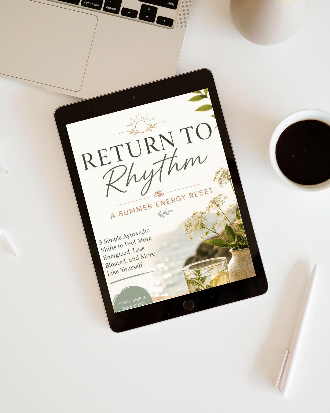 Digital device displaying a book titled "Return to Rhythm: A Summer Energy Reset" on a white desk, surrounded by a laptop, cup of coffee, a pen, and a vase with flowers.