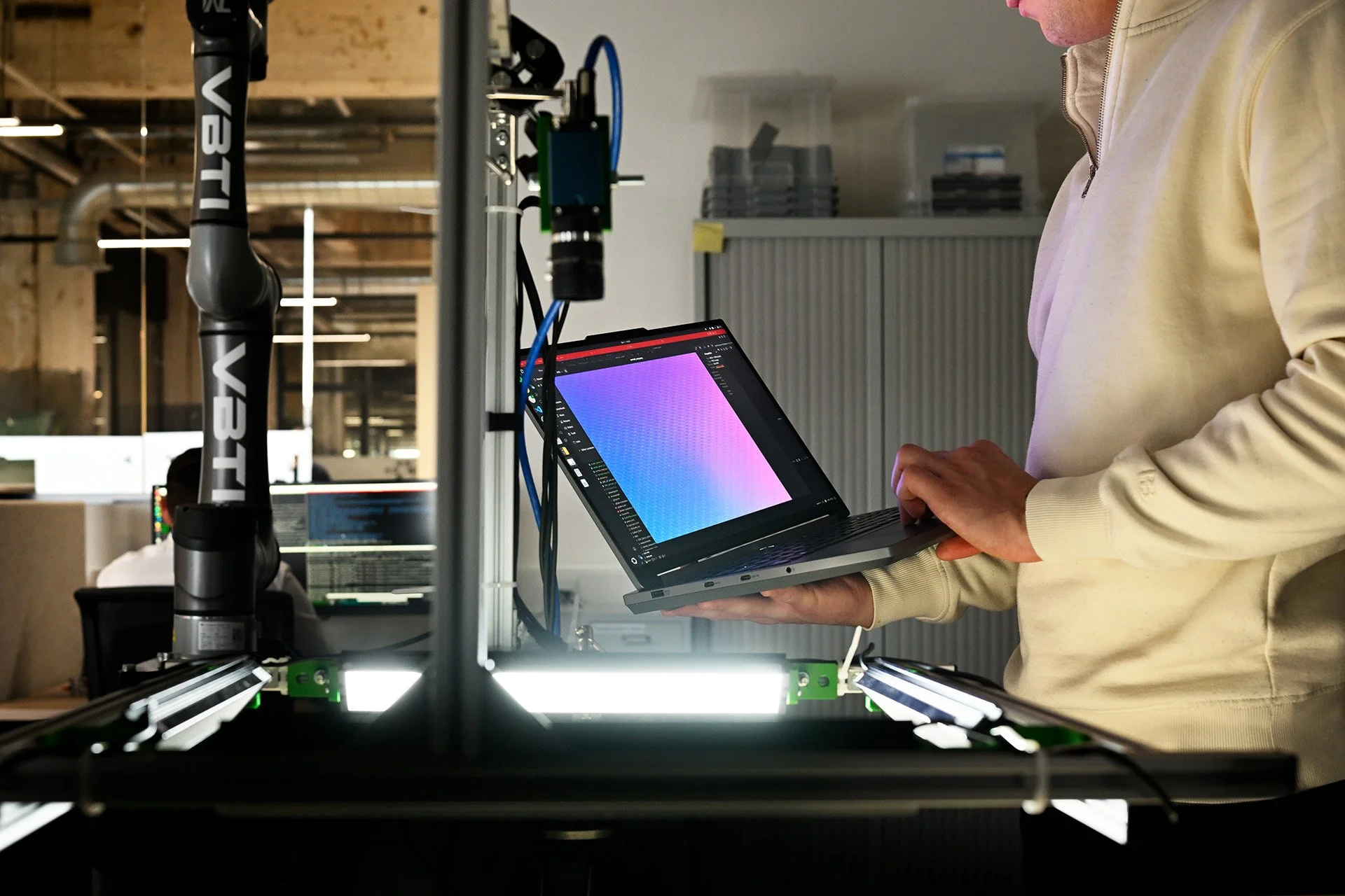 Person in a yellow hoodie operating a computer with a colorful gradient display, in a workshop or lab setting.
