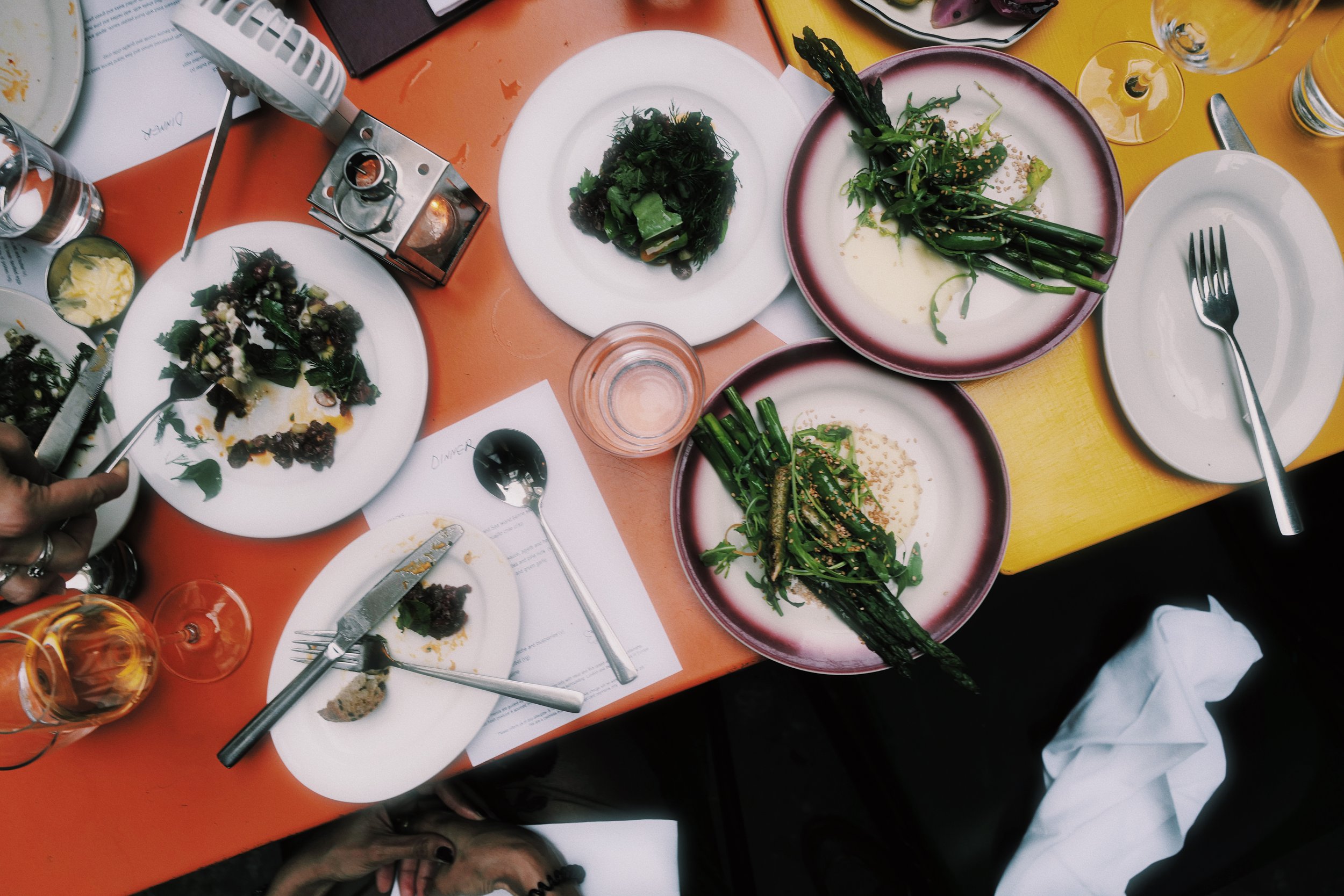 Overhead view of a table with partially eaten food dishes, empty plates, glasses of wine, and utensils at a casual dining setting.