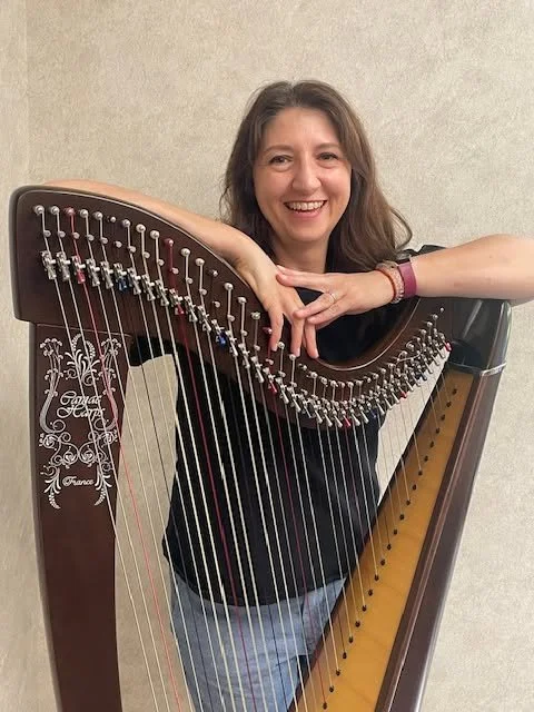 Woman with long brown hair smiling behind a harp