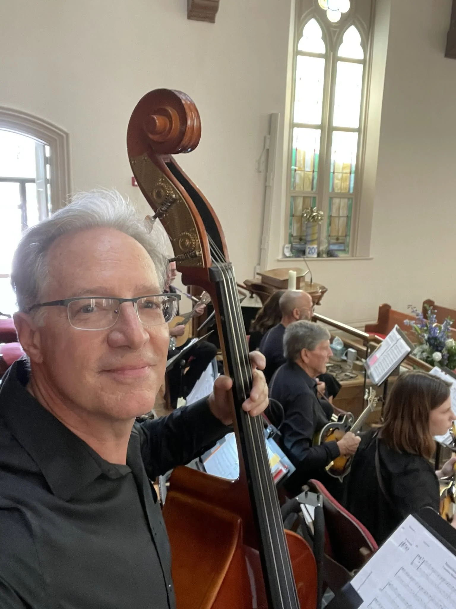 Man with short white-grey hair smiling and holding the neck of an upright bass