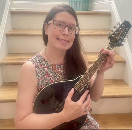 Woman with long, straight brown hair and glasses holding a mandolin