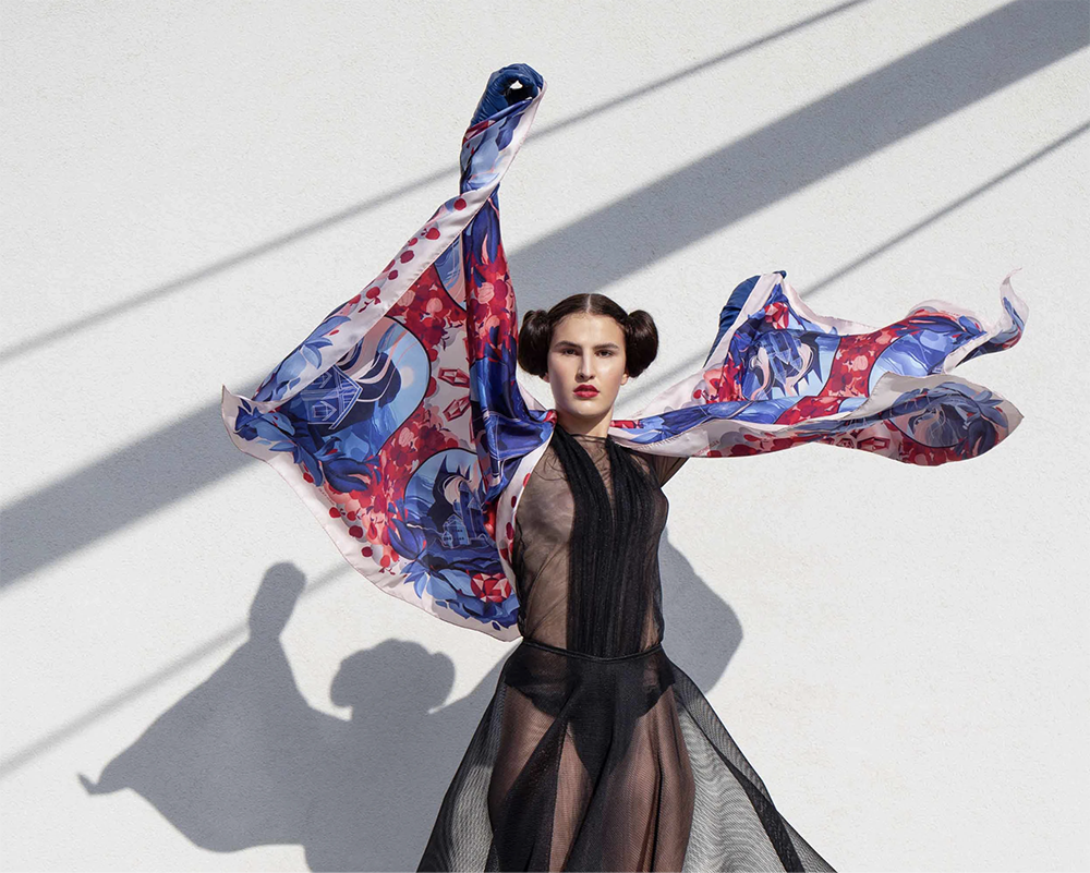 Model posing while wearing a Snow White–inspired scarf featuring ornate mirror motifs and fairytale-inspired apple and jewel patterns.
