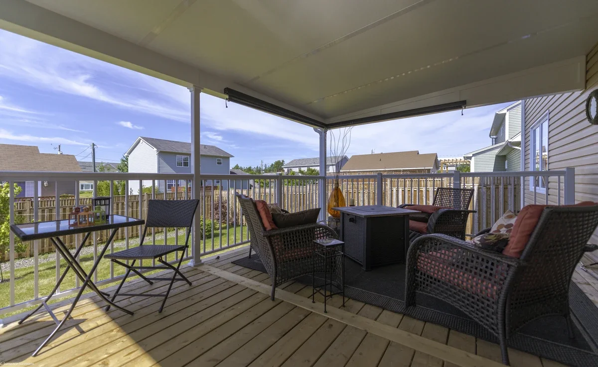 Covered porch with black wicker chairs and cushions, a small black table, a black outdoor rug, and a view of neighboring houses and blue sky.