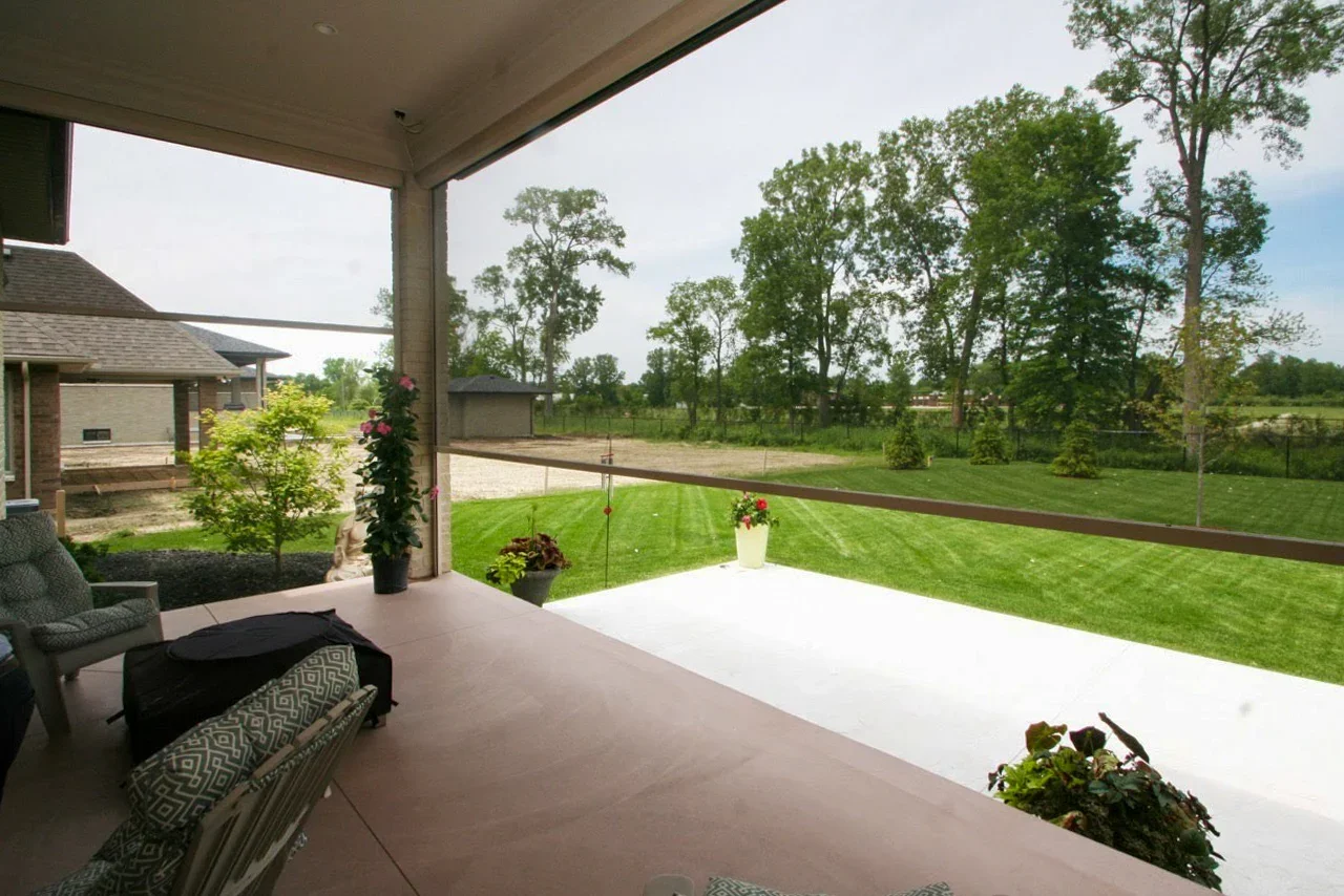 Covered patio with outdoor furniture, potted plants, and a view of a green backyard and trees.