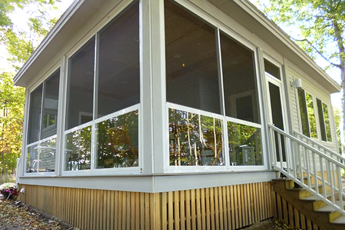 A house with a large screened porch, white framing, and stairs leading up to it, surrounded by trees.