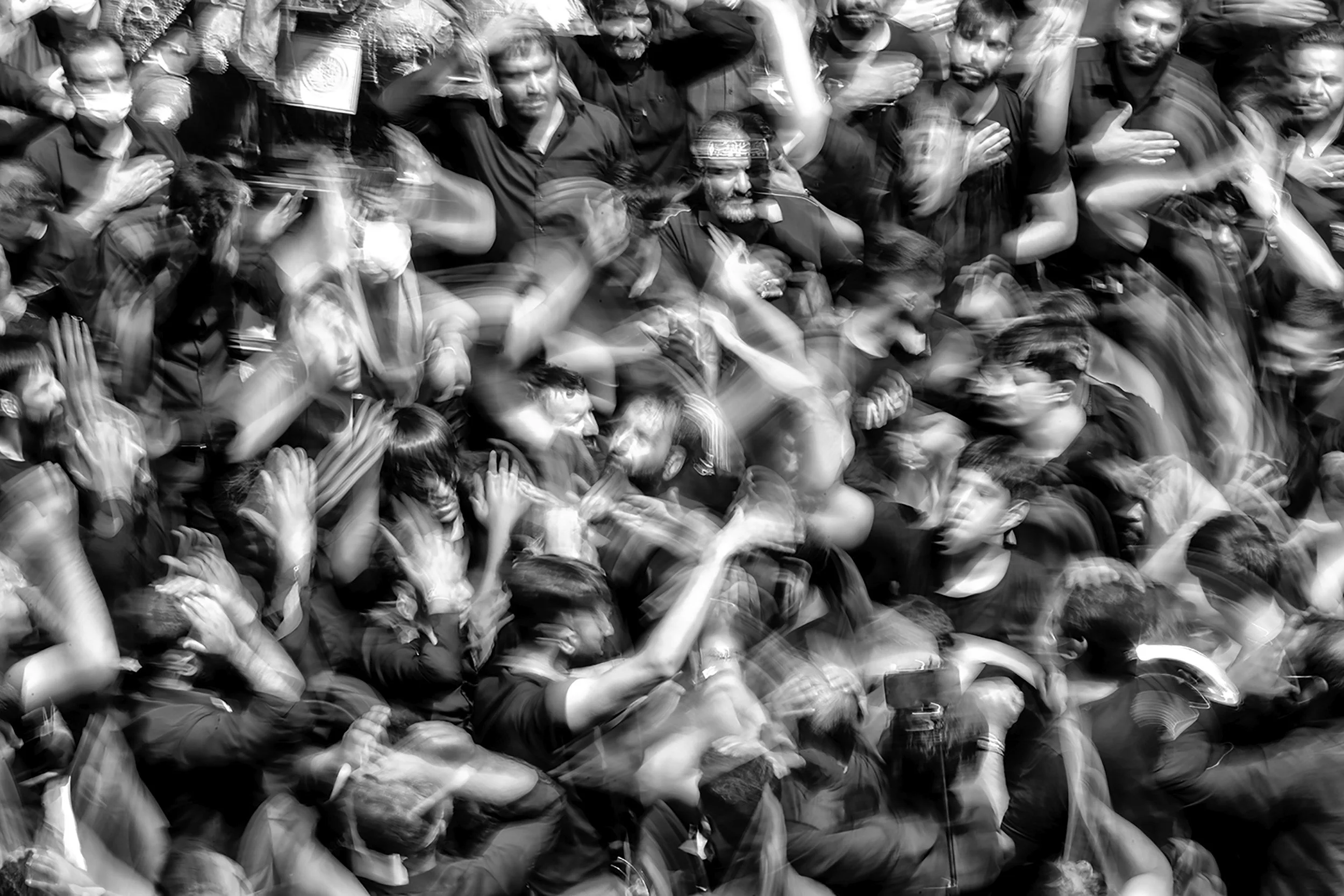 Black and white photo of a crowded group of people standing closely together, some with their hands on their chests, possibly participating in a ceremony or event.