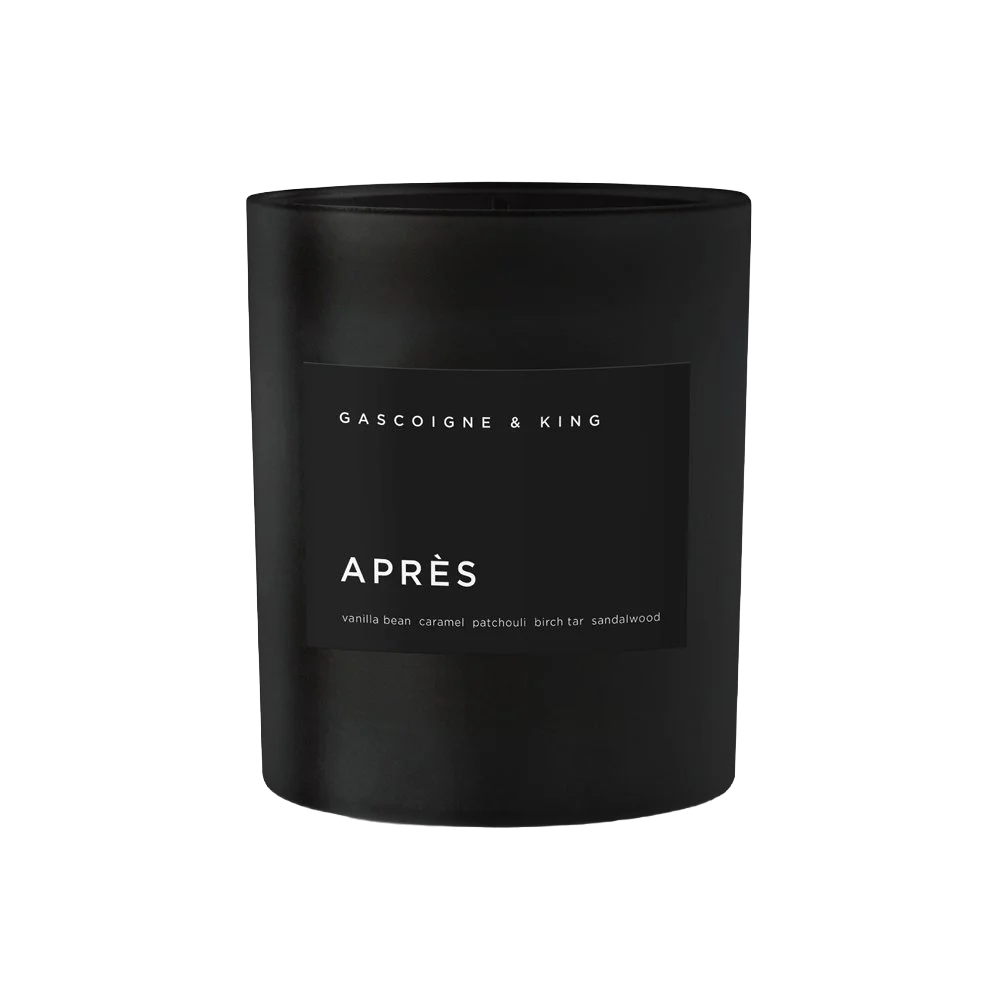 A black candle with a minimalist label indicating the scent as 'APRES' with notes of vanilla bean, caramel, patchouli, birch tar, and sandalwood.
