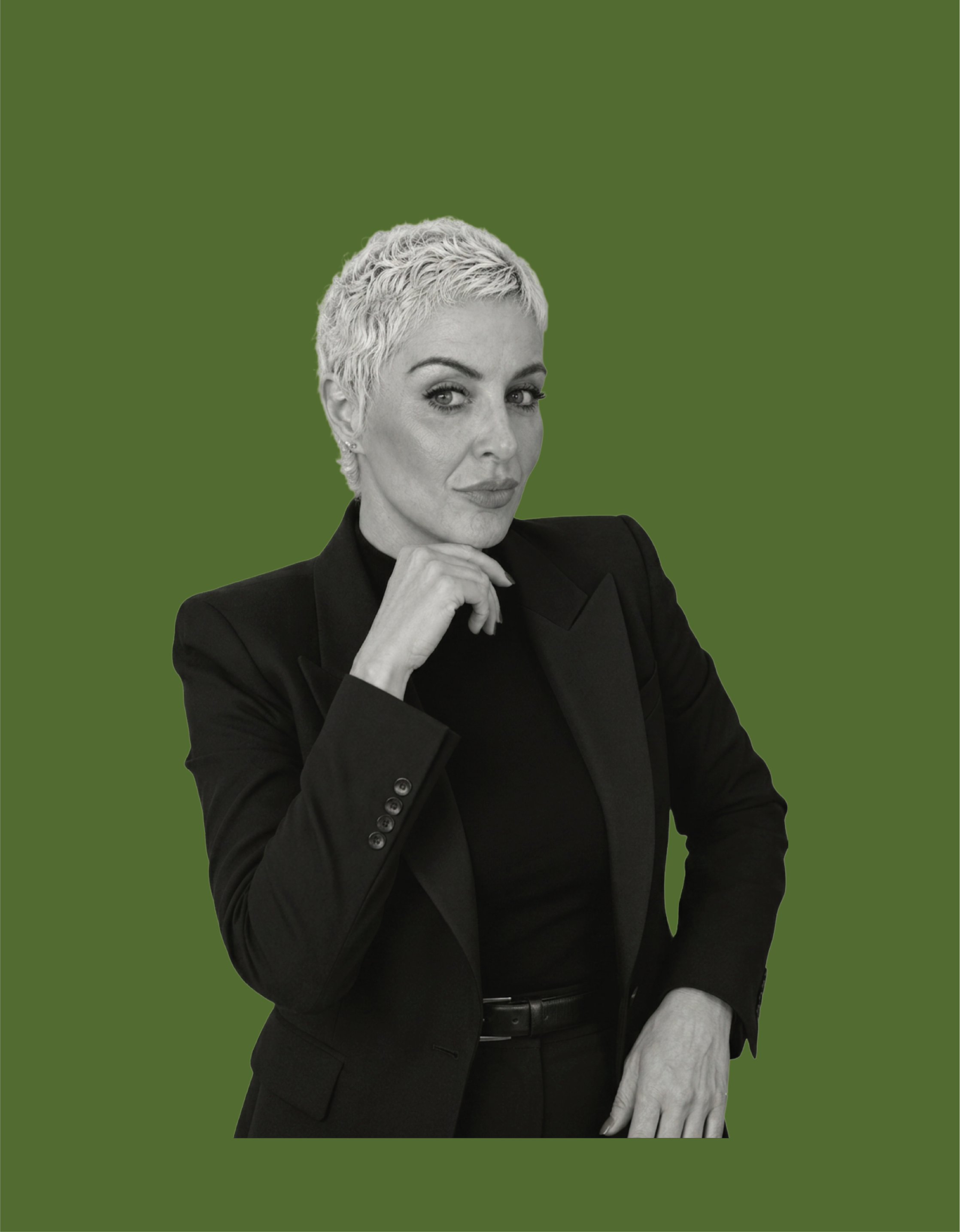 Black and white photo of a woman with short, curly hair, wearing a dark blazer, looking confidently at the camera with her hand near her chin, against a solid green background.