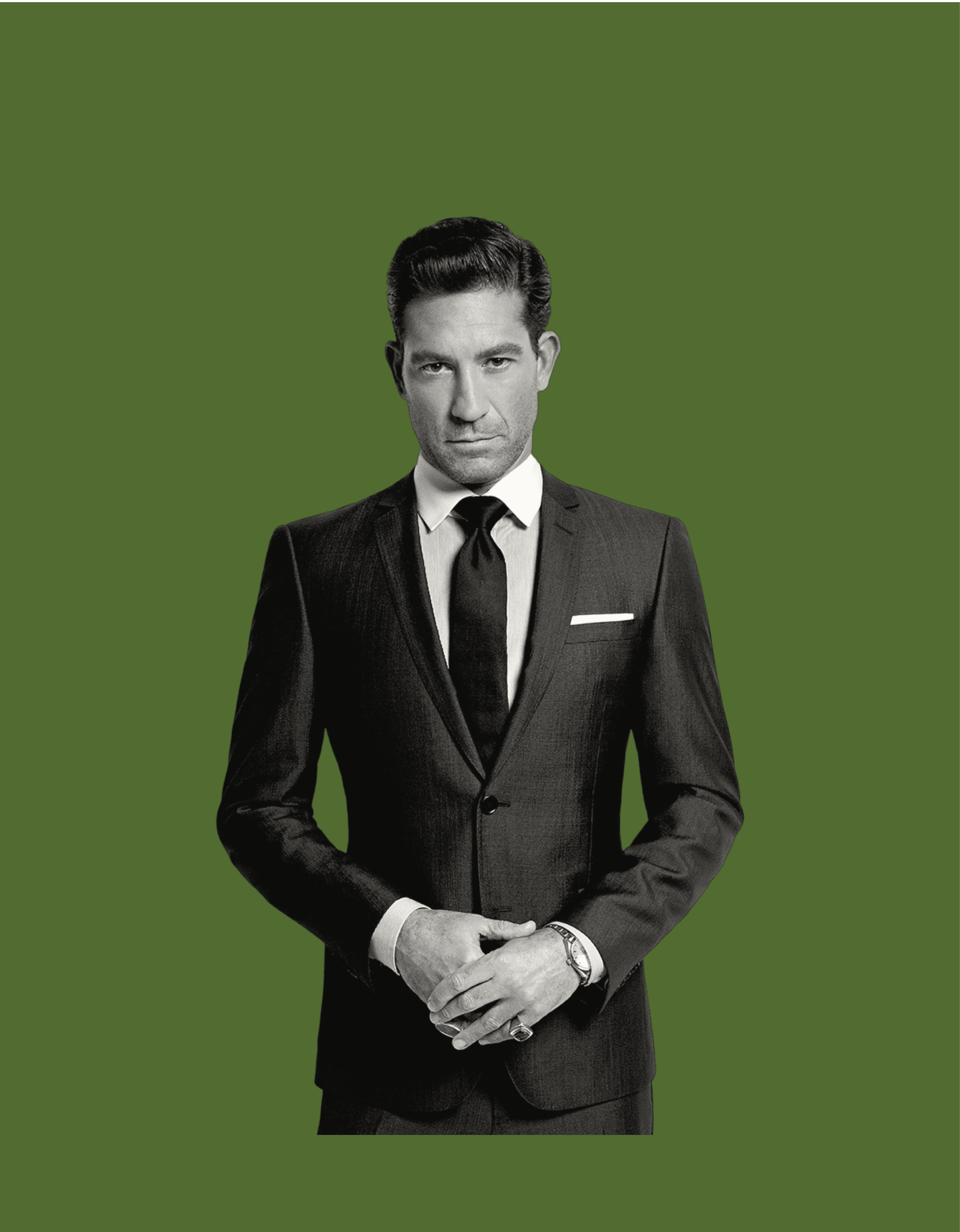 Black and white image of a man in a suit with a tie, holding his hands clasped in front of him, against a solid green background.