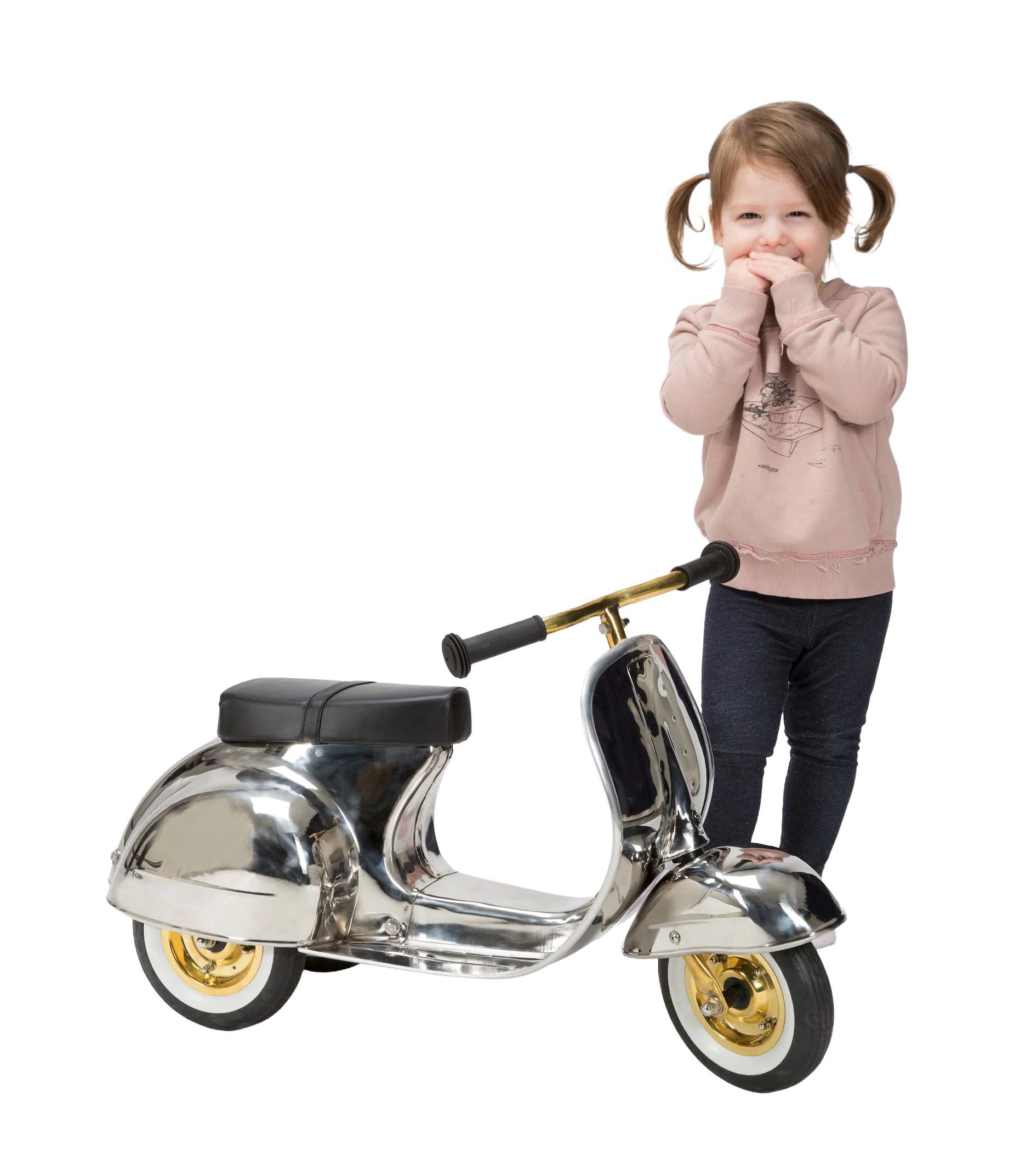 A young girl with pigtails smiling and covering her mouth with her hands, standing beside a shiny silver scooter with gold wheels and a black seat.