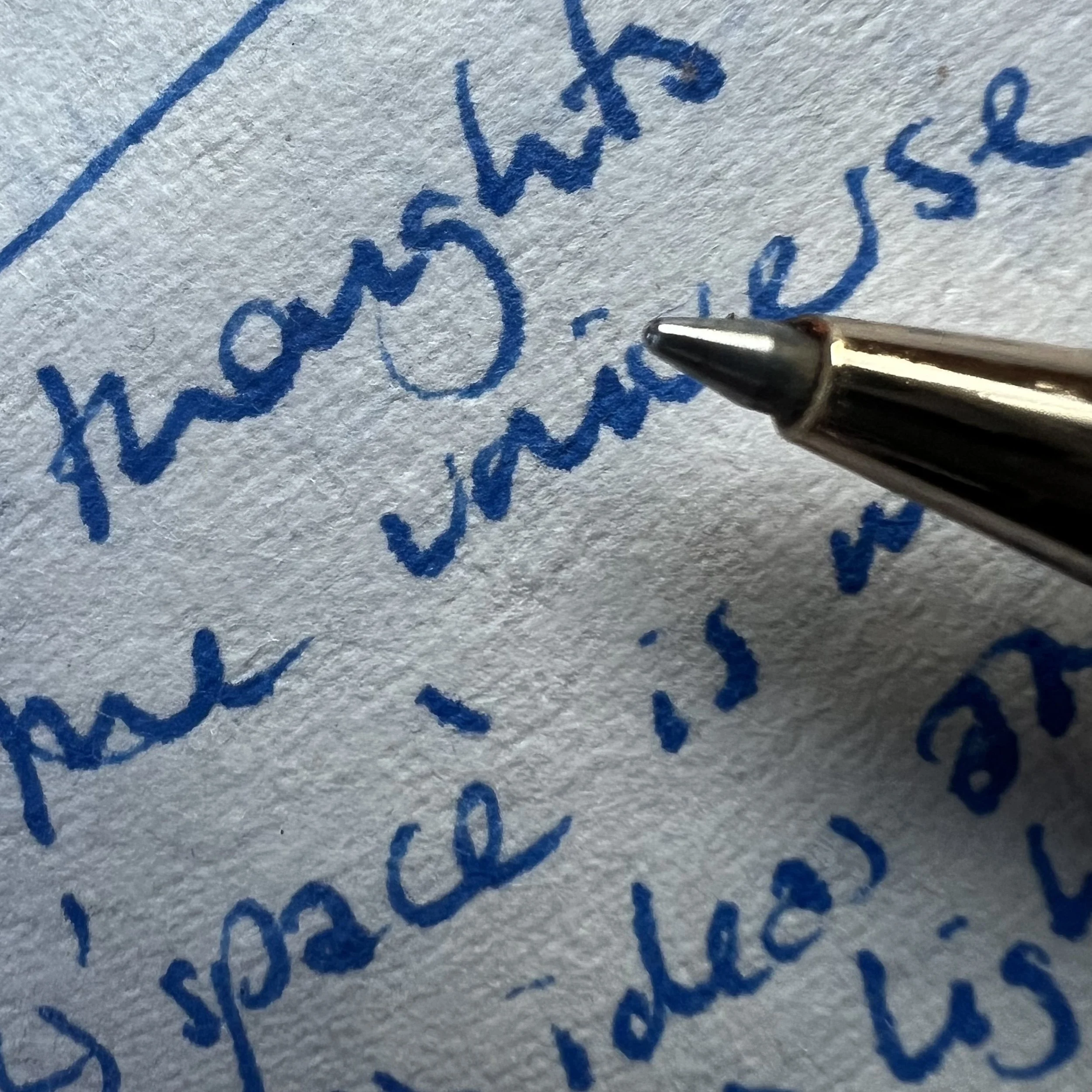 Close-up of a blue ballpoint pen writing on a textured white paper with handwritten cursive text.