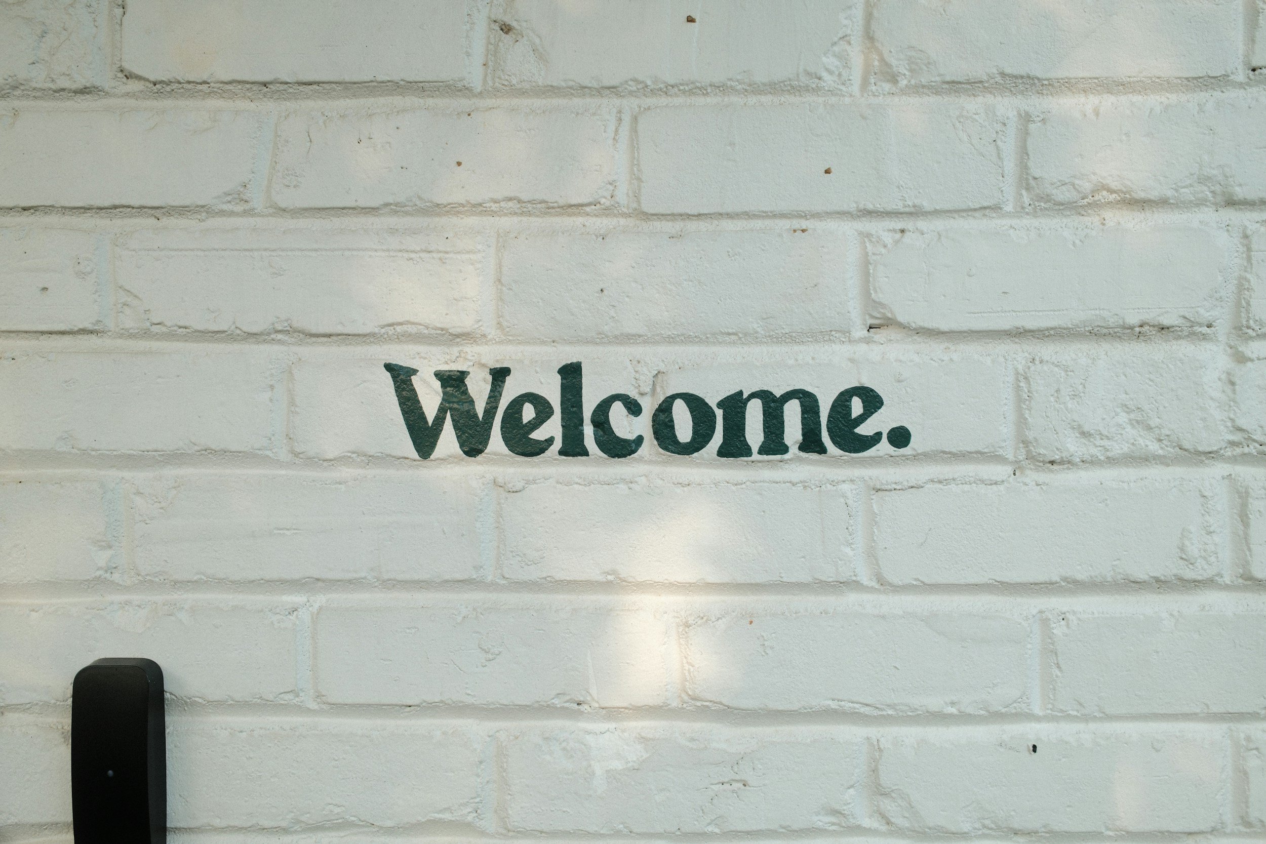 White painted brick wall with the word 'Welcome' painted in green text.