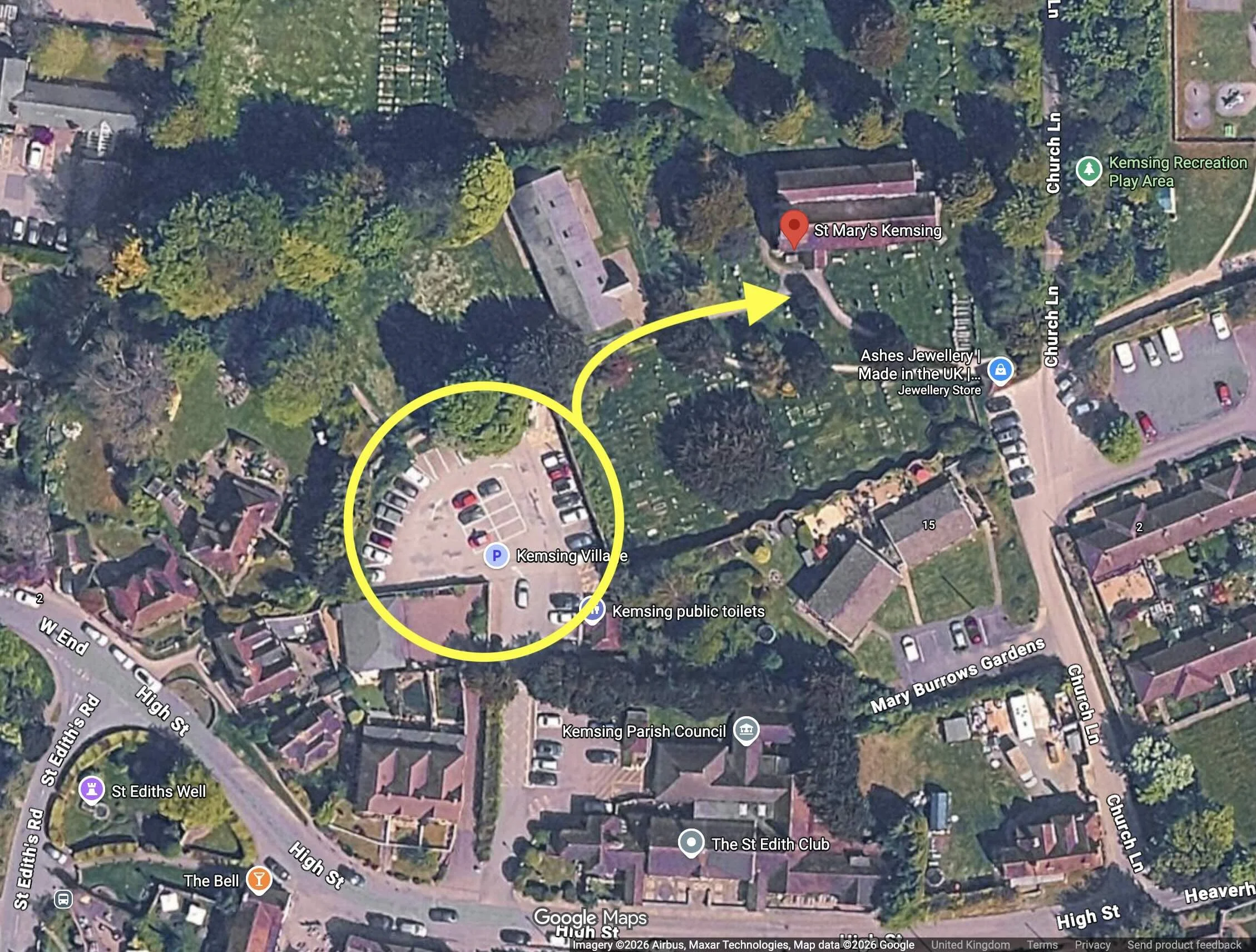 Aerial view of Kemsing village showing parking lot, church, cemetery, and surrounding trees and buildings in England.