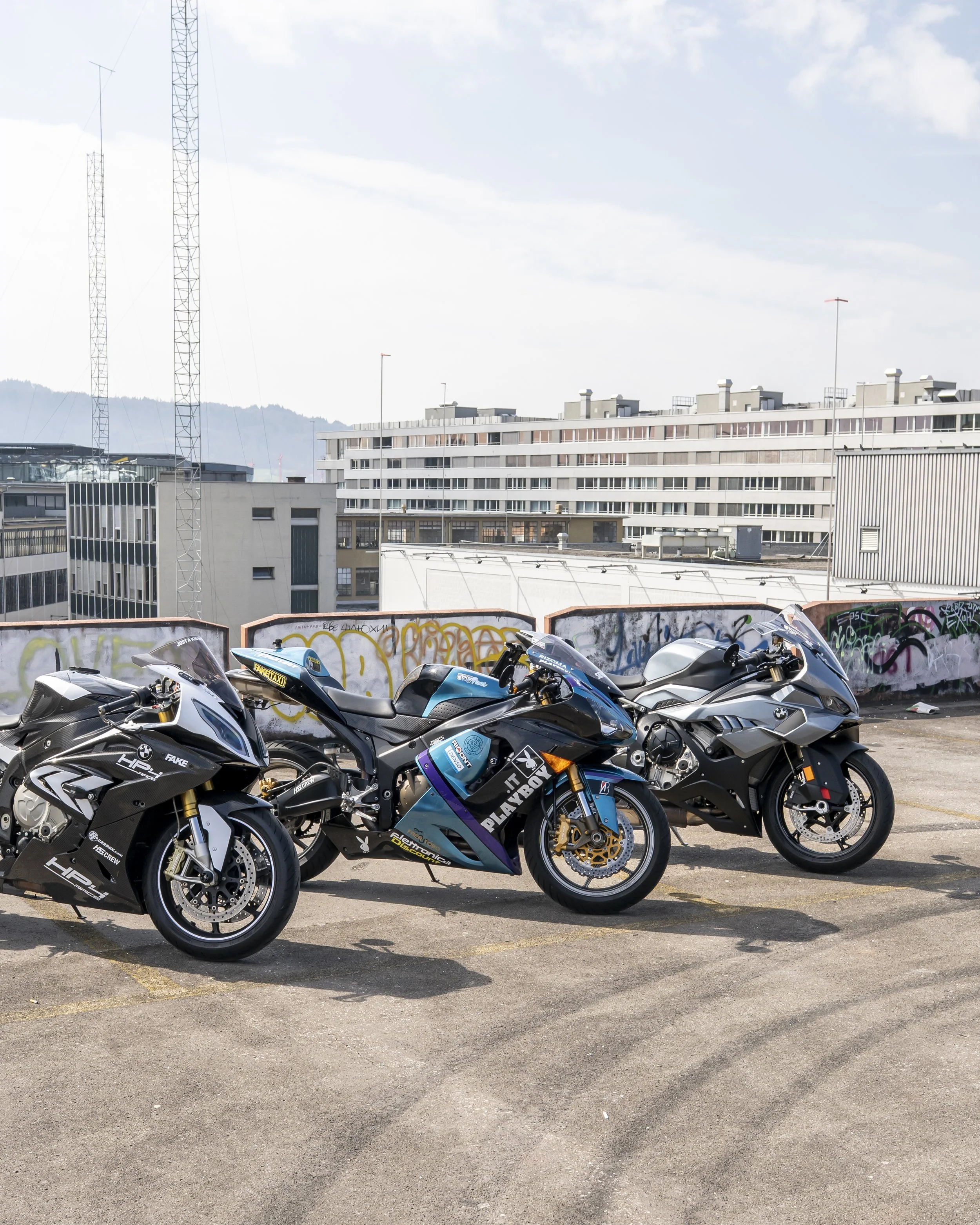 Four sport motorcycles parked on a rooftop with a graffiti-covered wall in the foreground and city buildings in the background.