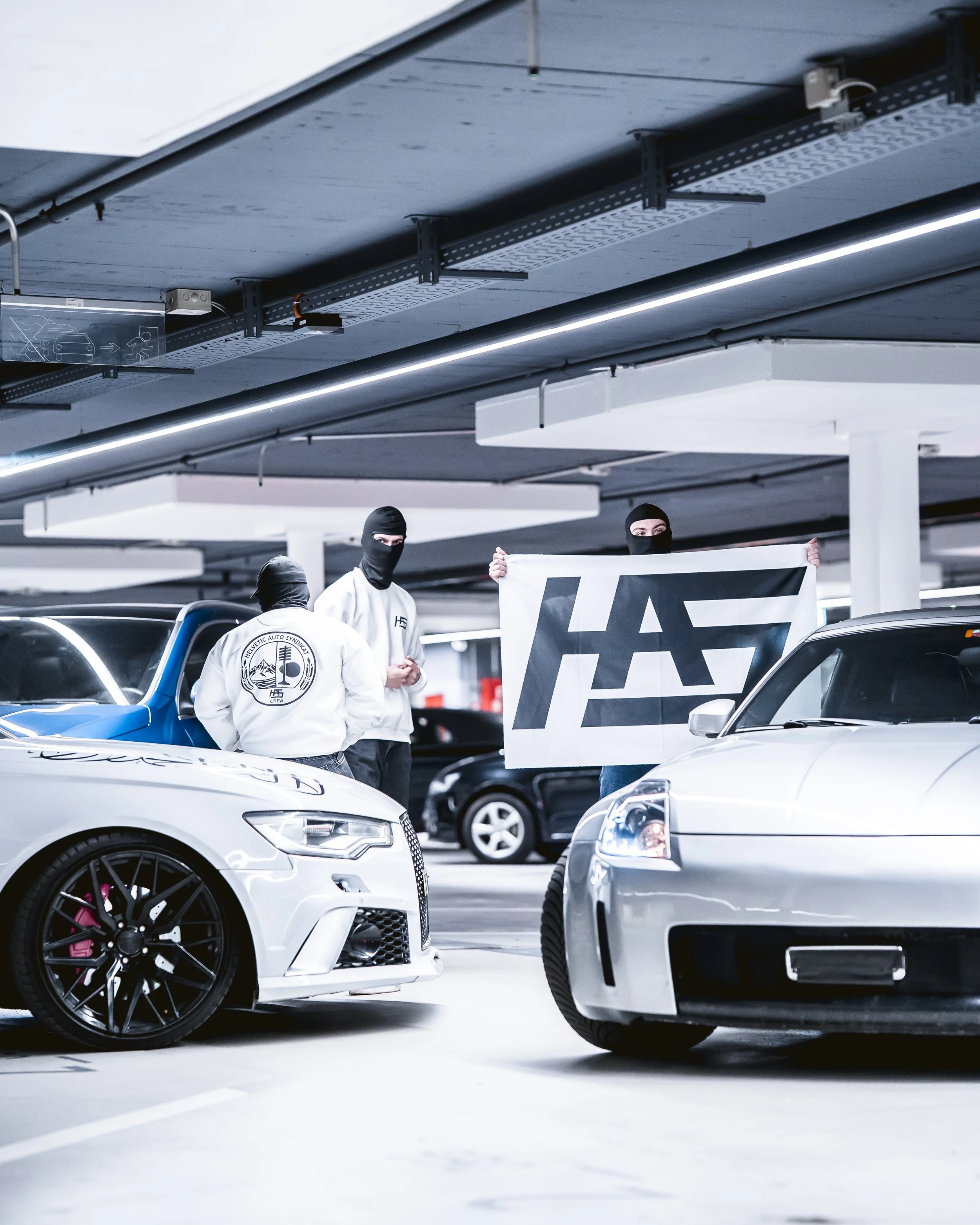 People wearing masks holding a banner in parking garage surrounded by luxury cars.