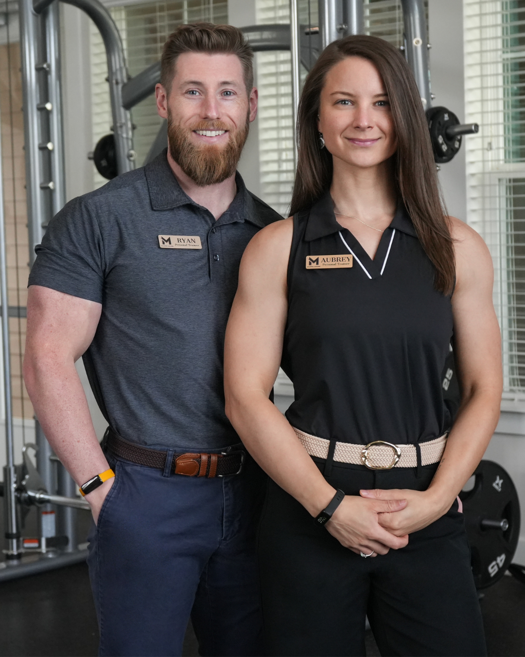 Two fitness trainers, Ryan and Aubrey, standing in a gym with exercise equipment behind them.
