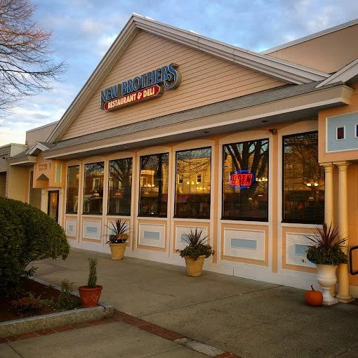 Exterior of a restaurant called 'New Brothers,' with large windows, potted plants, and a neon 'Open' sign in the window.