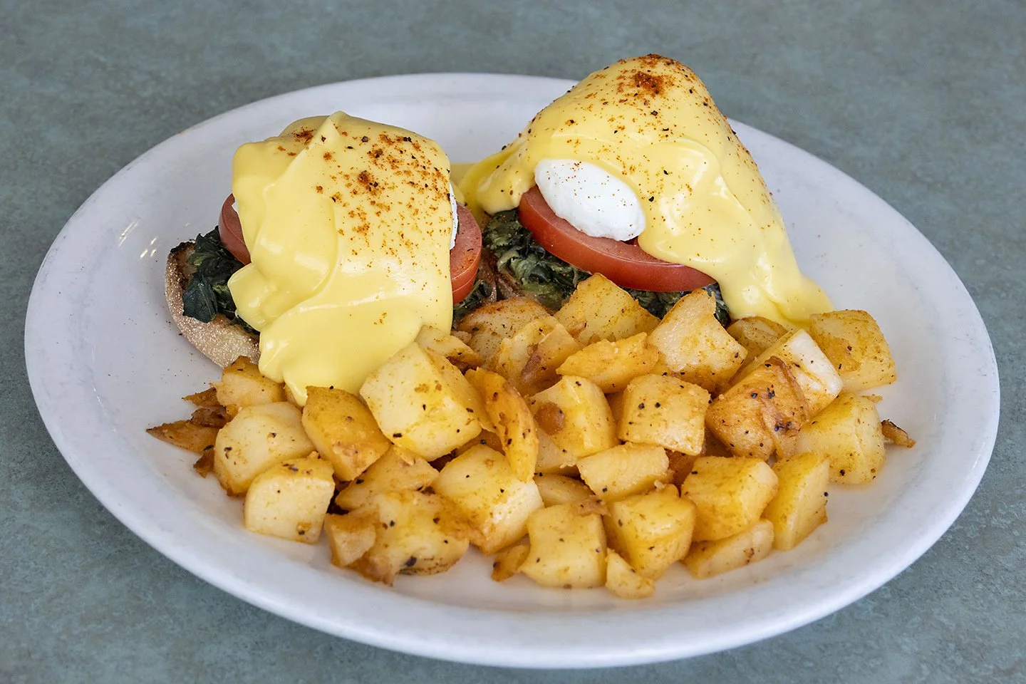 Plate with two eggs Benedict, diced hash browns, slices of tomato, and spinach on toast