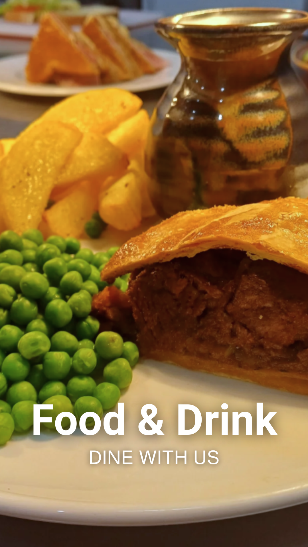 Plate of food including a piece of roasted meat with a crispy crust, green peas, potato wedges, and a small bowl of dark sauce or gravy, with a blurred background of additional food items.
