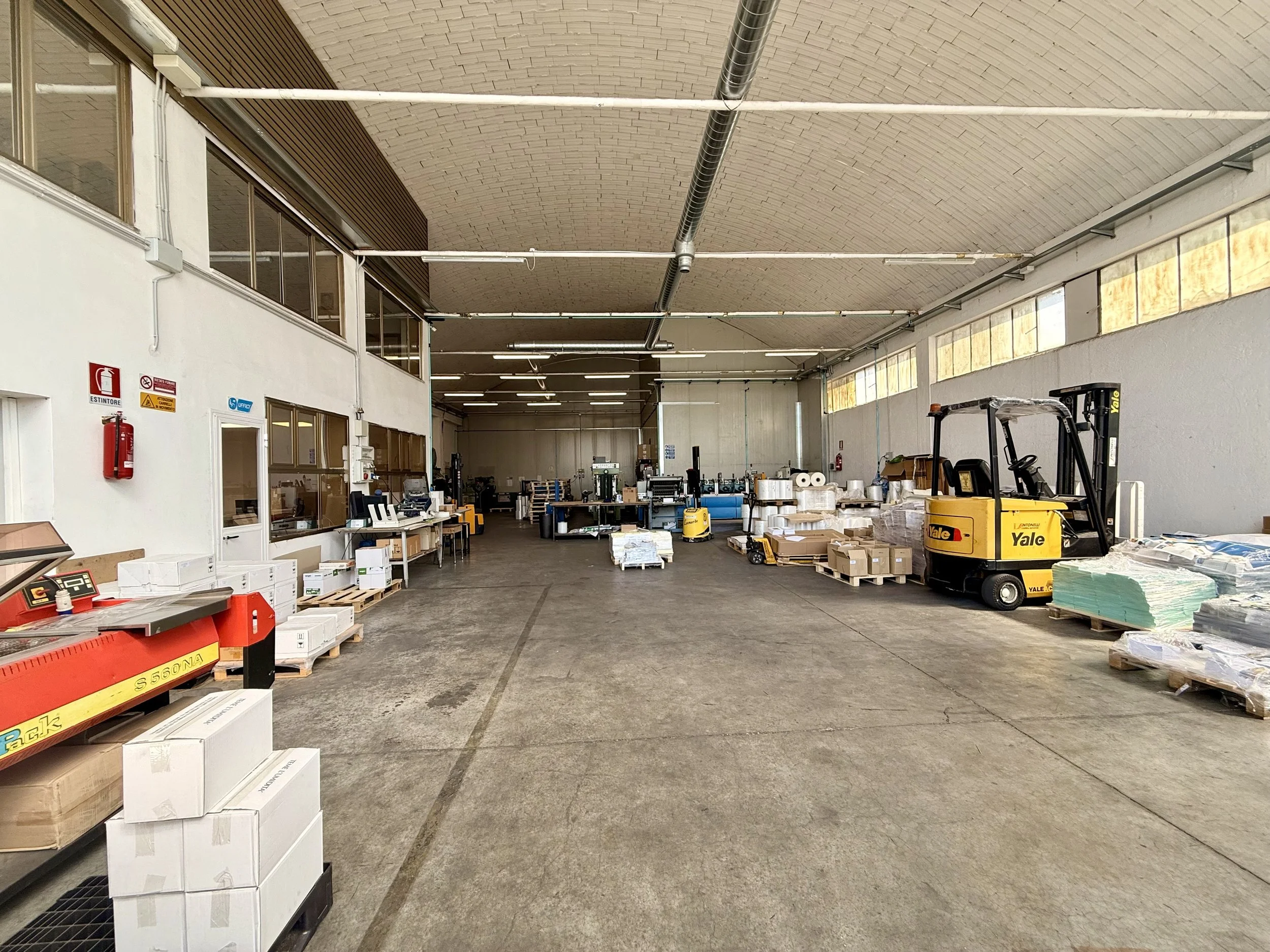 Interno di un magazzino o un'area di stoccaggio con scaffali, materiali, e un carrello elevatore giallo Yale
