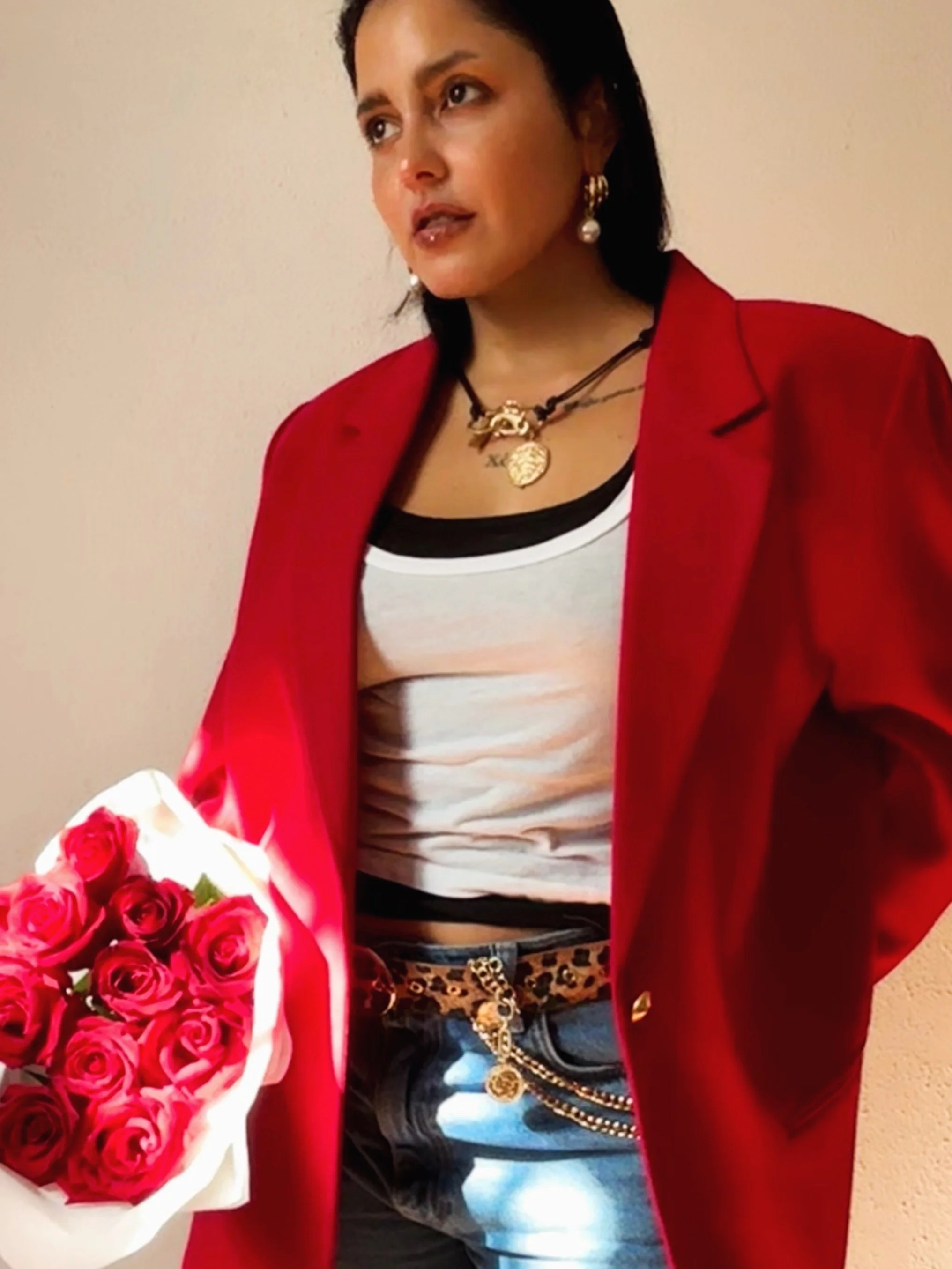 Woman wearing a red coat, black and white striped crop top, leopard print shorts, gold jewelry, holding a bouquet of red roses.