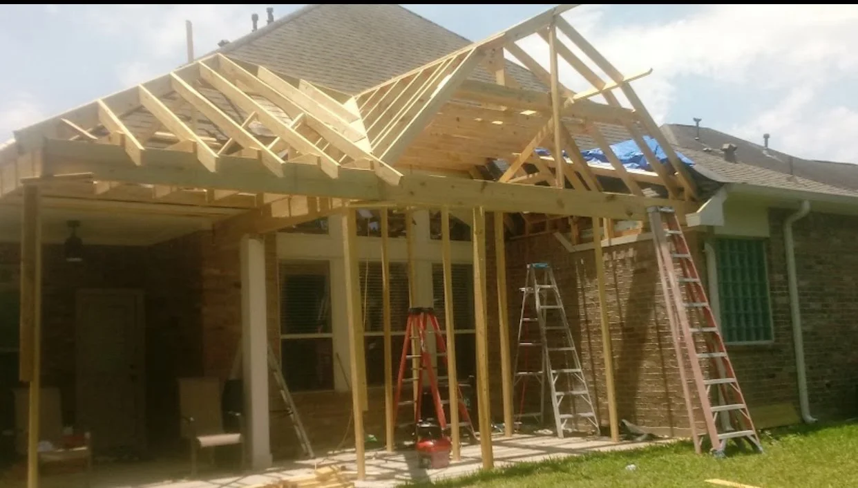 Construction of a wooden porch extension on a brick house with ladders leaning against the structure.