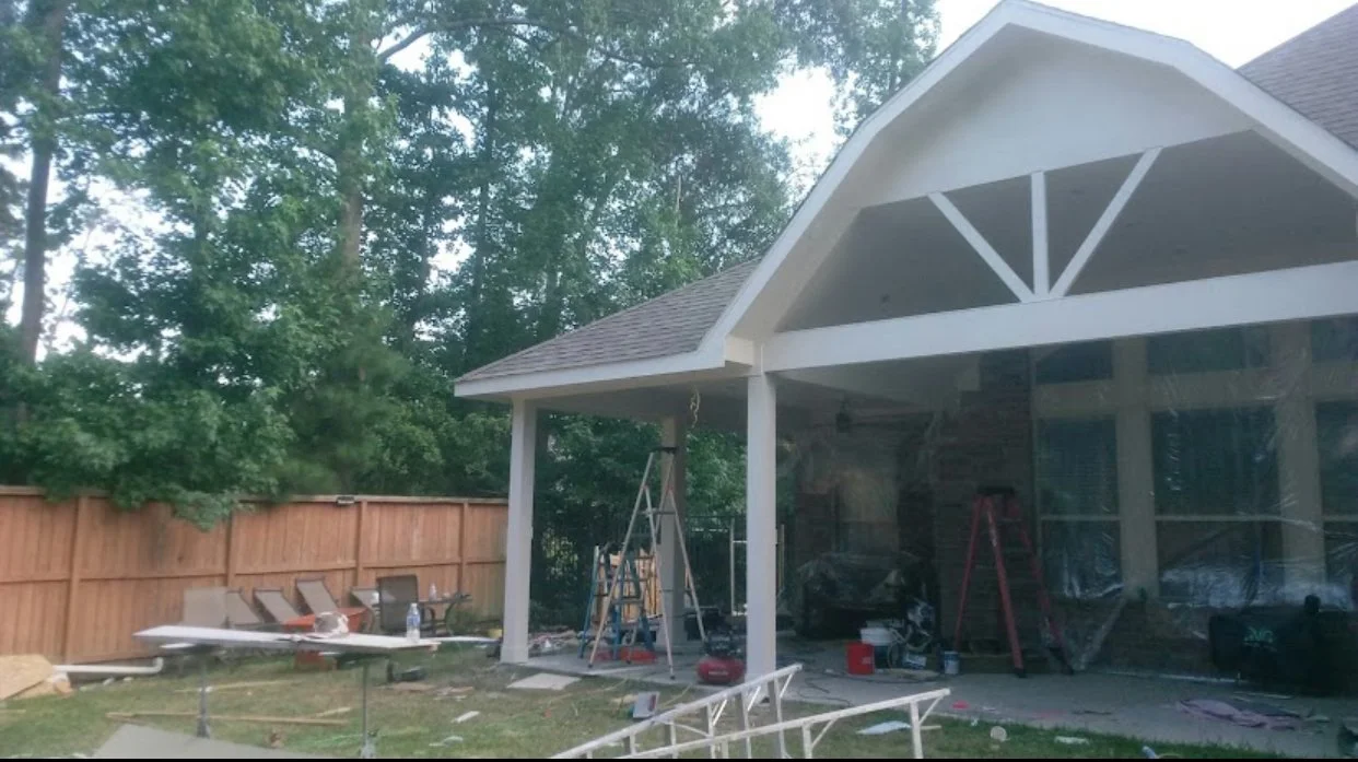 Back porch of house undergoing renovation, with ladders, construction materials, and furniture covered in plastic.