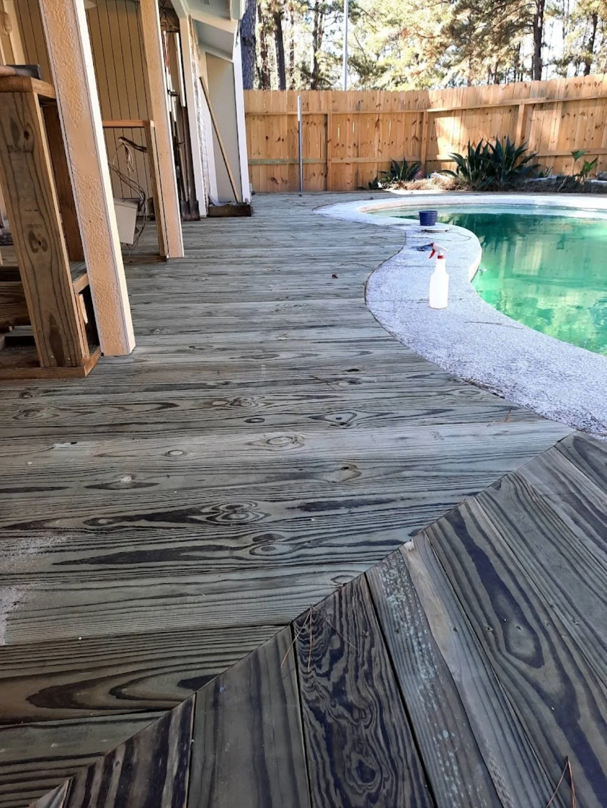View of a backyard with a wooden deck, a partially constructed house, and a swimming pool with cleaning supplies on the edge.