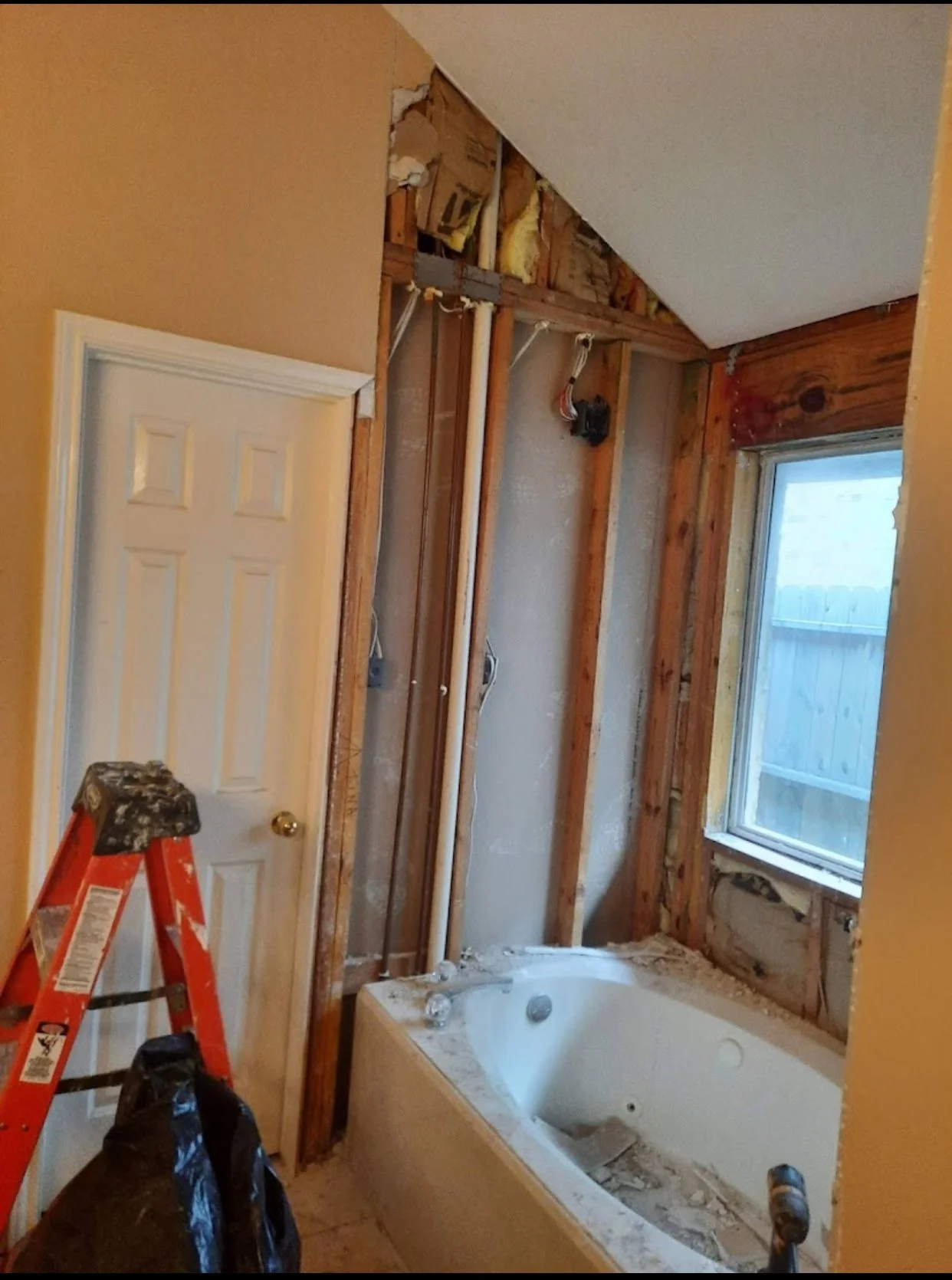 Bathroom undergoing renovation with exposed wall studs, a bathtub, a window, and a ladder.