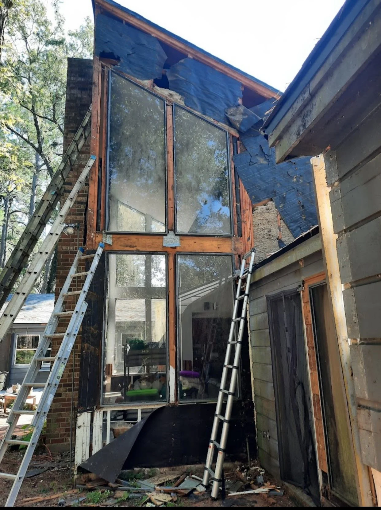 Construction of a new glass extension to a house, with ladders leaning against the structure and protective blue sheeting hanging from the roof.