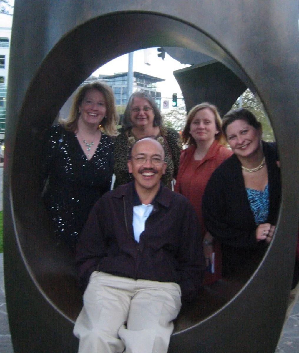 A group of five people posing together inside a large circular sculpture, with an urban background of buildings and streetlights.
