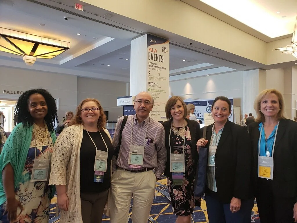 Six people posing together at a conference, with a banner in the background reading 'ALA Events' indicating a professional gathering.