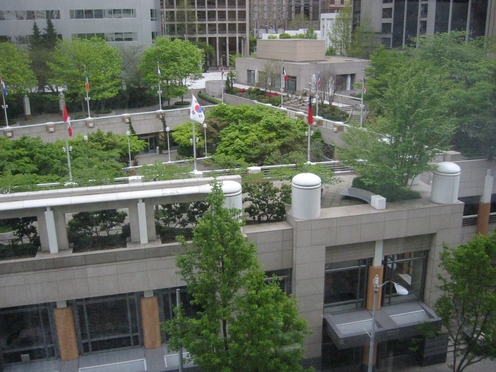 Urban rooftop garden with trees, flags, and modern buildings in the background.