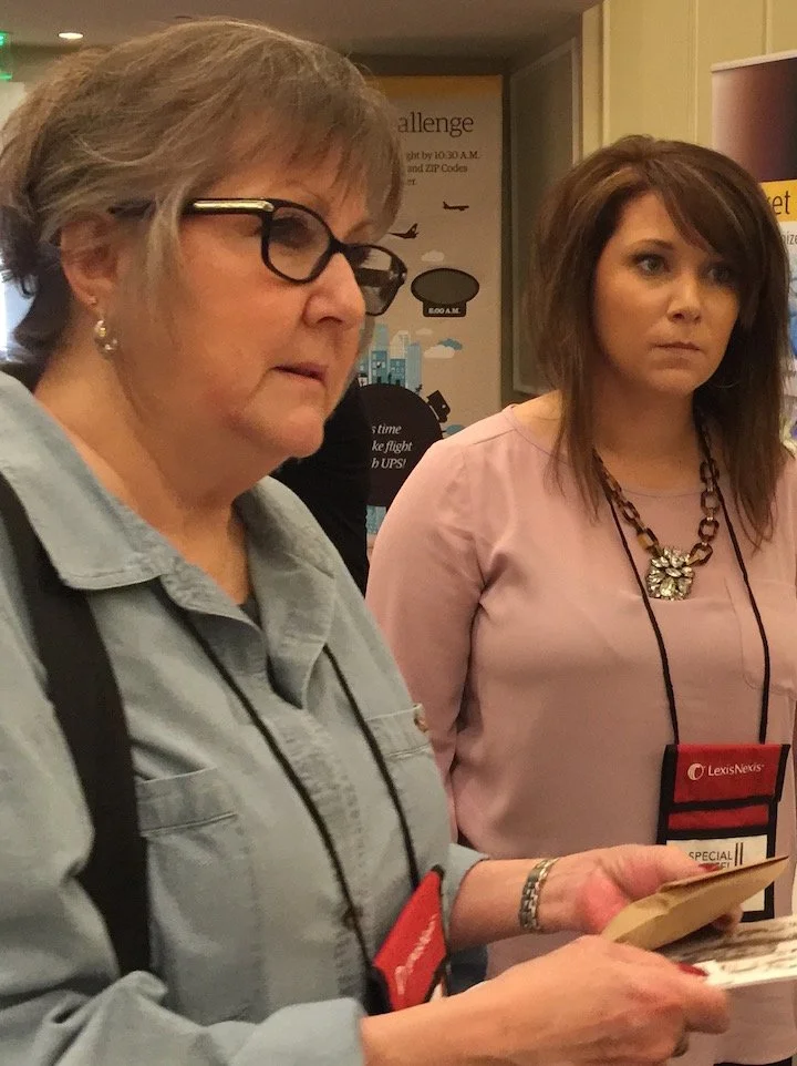Two women looking at papers or brochures at an indoor event or conference.