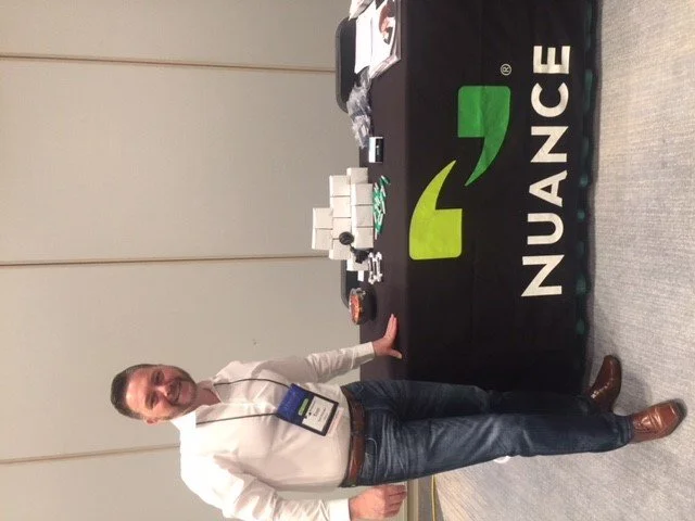 A man standing next to a table with a Nuance logo, displaying promotional items and boxed products.