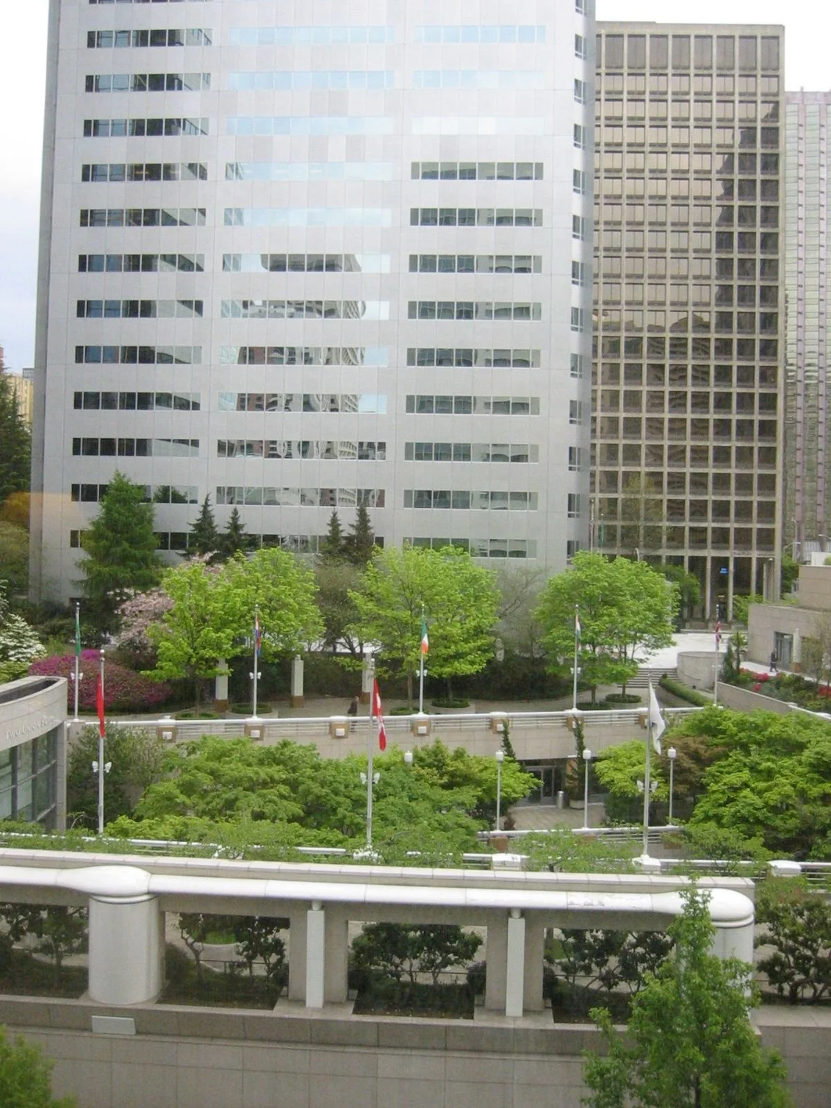 View of cityscape with modern office buildings, trees, and flagpoles with flags in the foreground.