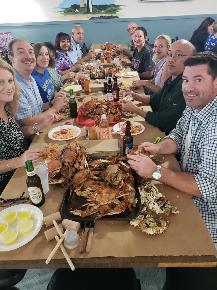 Group of people sitting at a long table enjoying a seafood feast with crab, lobster, and drinks.