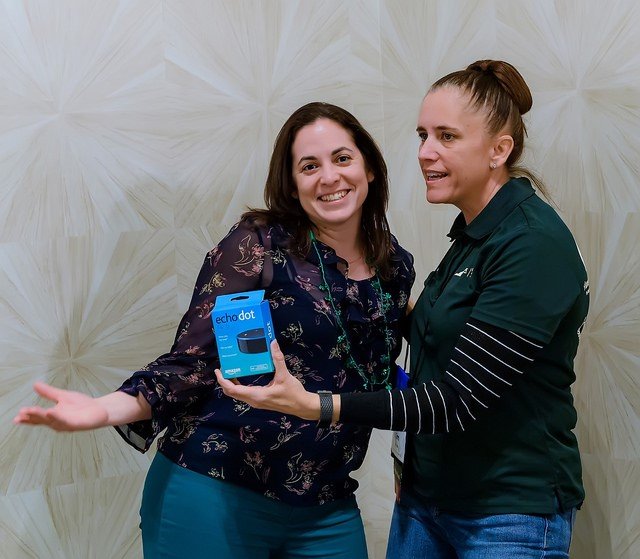 Two women standing close together indoors, smiling; one holding a box of a health monitoring device.