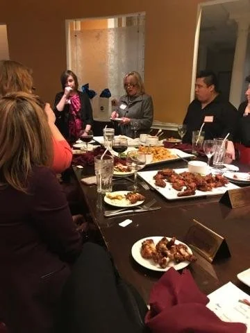 People gathered around a dining table with various dishes and drinks, engaged in conversation.