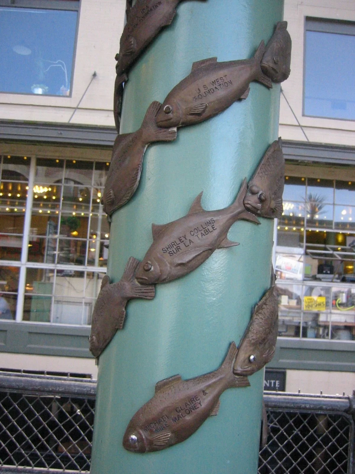Decorative pole with metal fish sculptures attached, each with engraved names.