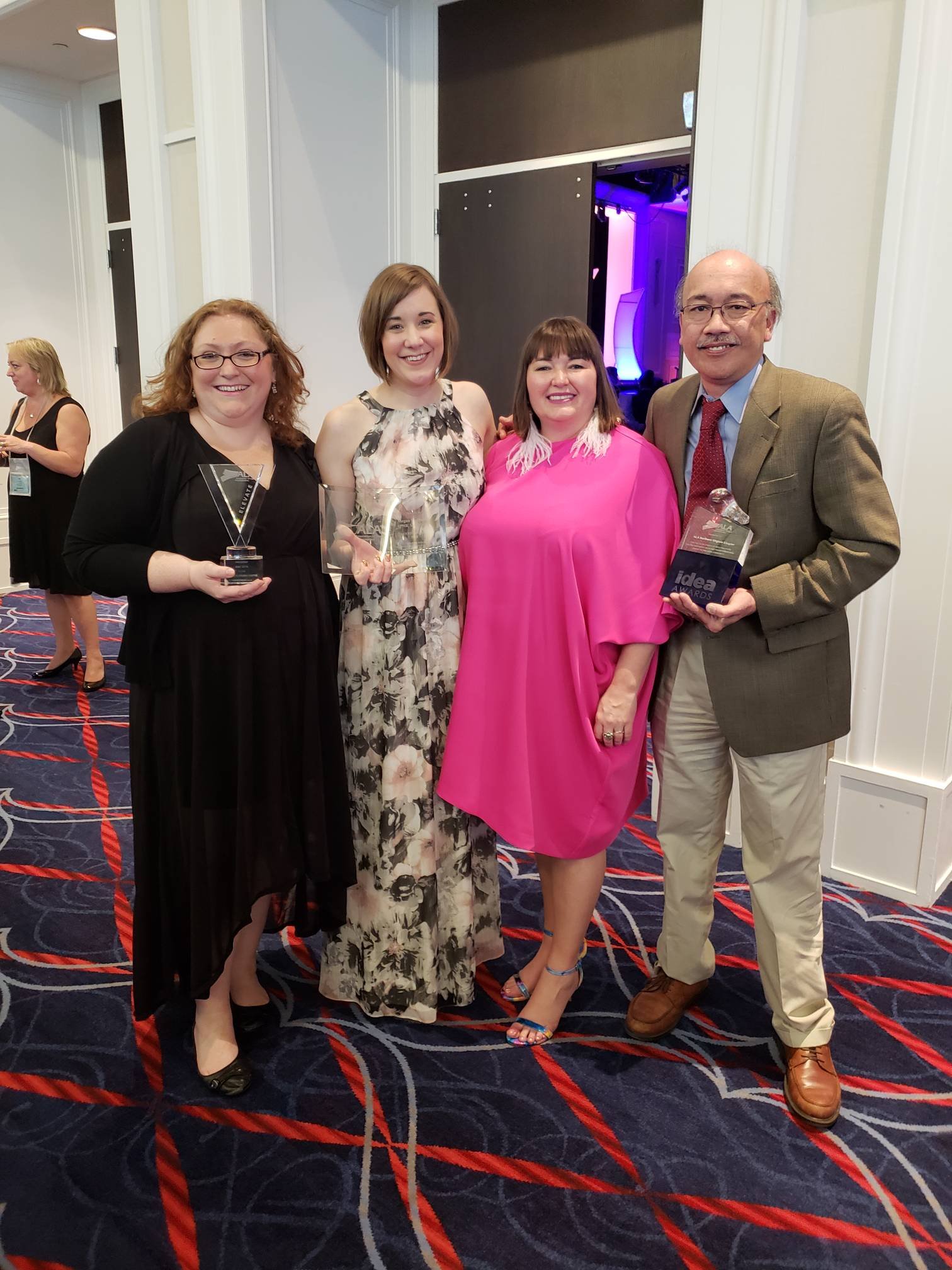 Four people standing together at an awards event, holding trophies, in a decorated event space.