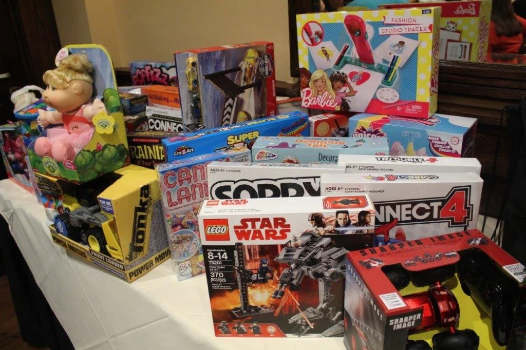 Table with various children's toys including a doll, toy truck, LEGO Star Wars set, board games, and arts and crafts kits.