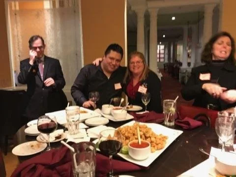 Group of four people smiling and socializing at a dinner party with food and drinks on the table.