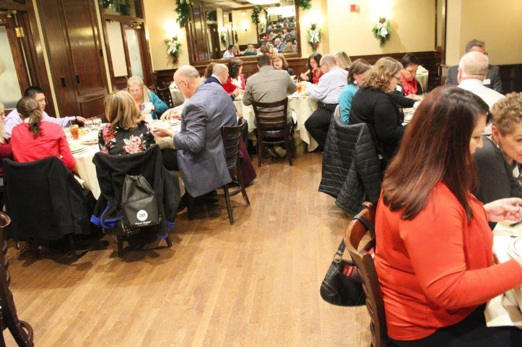 People dining at tables in a warmly decorated restaurant during a holiday gathering.