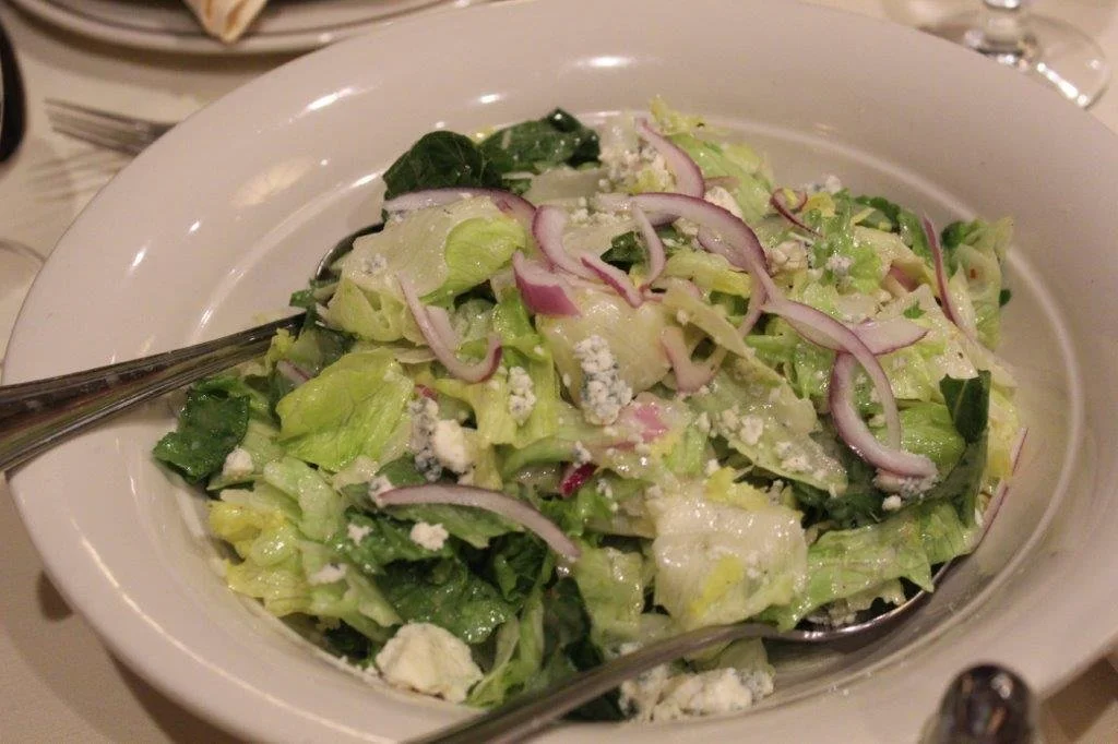 A bowl of chopped lettuce salad with red onion slices, crumbled blue cheese, and mixed greens.